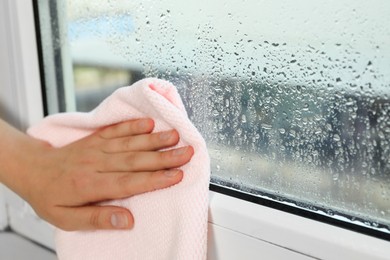 Photo of Woman wiping window glass with drops of condensate indoors, closeup. Space for text