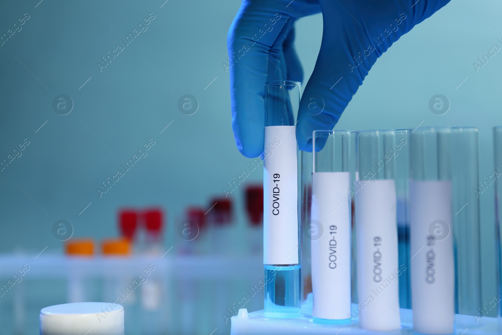 Photo of Scientist taking test tube with label Covid-19 from holder on blurred background, closeup. Space for text