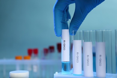 Photo of Scientist taking test tube with label Covid-19 from holder on blurred background, closeup. Space for text