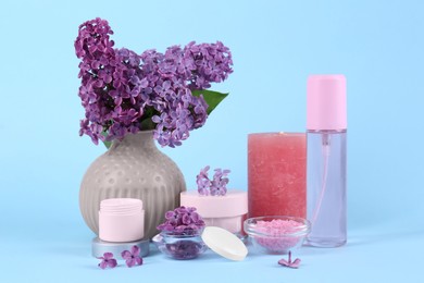 Cosmetic products and lilac flowers on light blue background