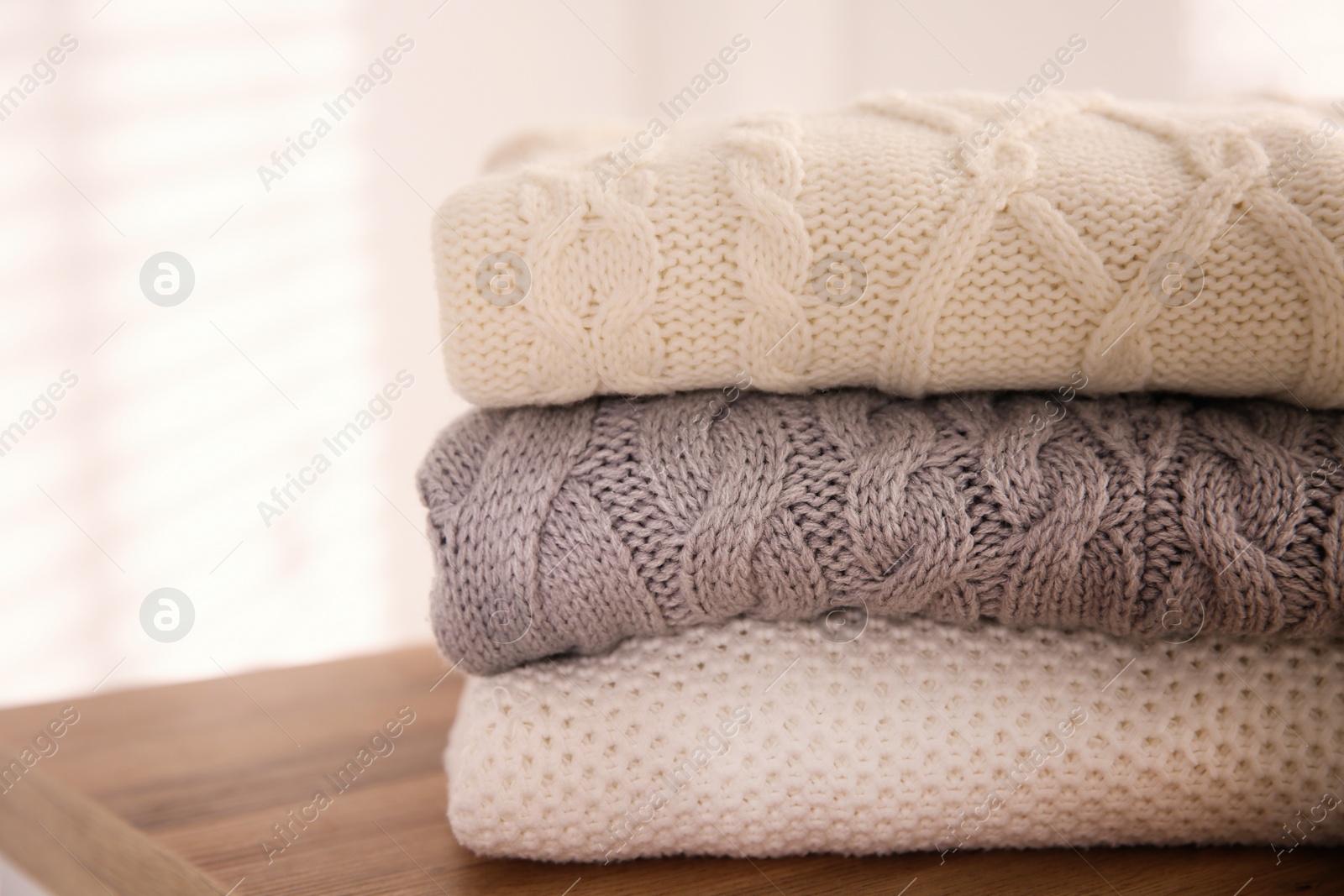 Photo of Stack of folded warm sweaters on wooden table indoors, closeup