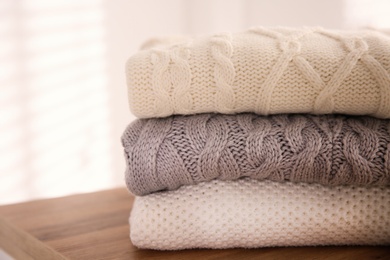 Stack of folded warm sweaters on wooden table indoors, closeup