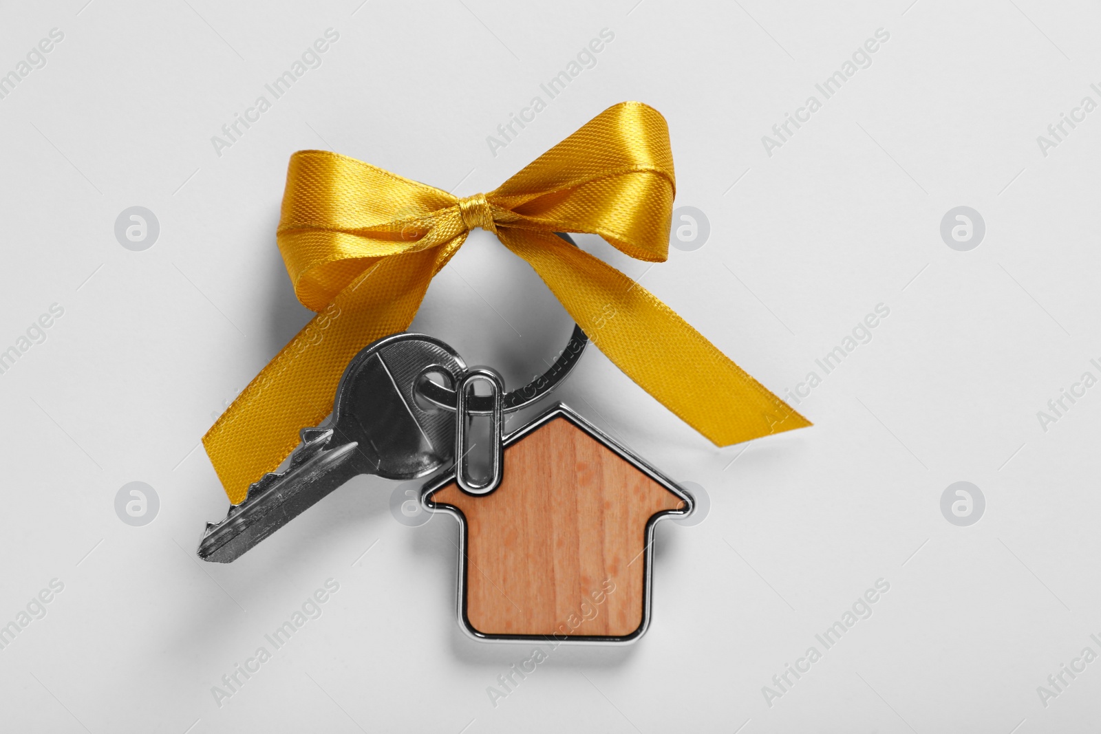 Photo of Key with trinket in shape of house and yellow bow on light grey background, top view. Housewarming party