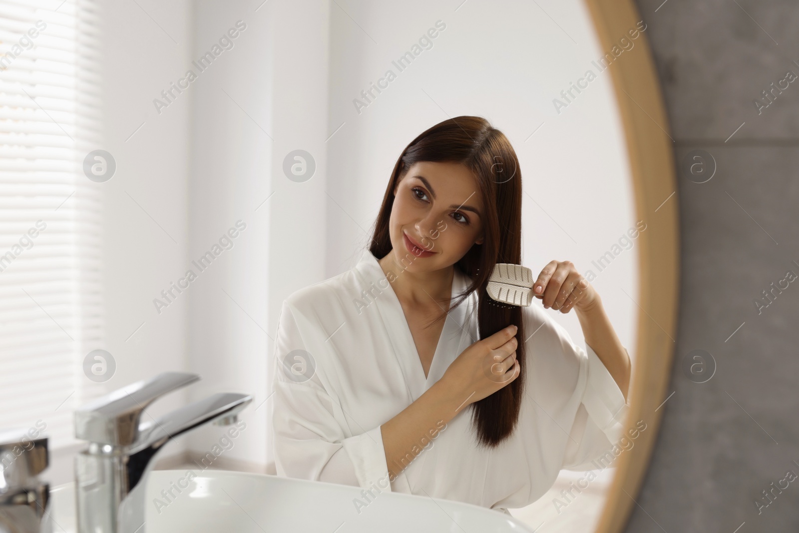 Photo of Beautiful woman brushing her hair near mirror in bathroom