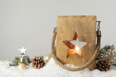 Composition with wooden Christmas lantern on snow against light grey background, space for text