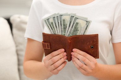 Photo of Woman holding brown leather wallet with dollar bills indoors closeup. Money exchange