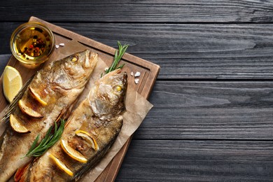 Photo of Tasty homemade roasted perches on black wooden table, top view and space for text. River fish