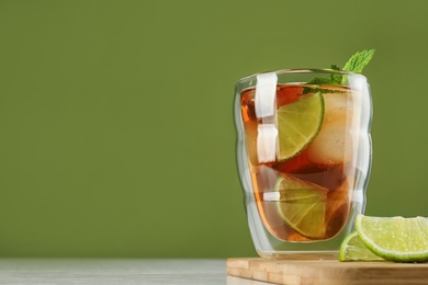 Photo of Glass of tasty ice tea with lime on white table against green background, space for text