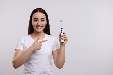 Photo of Happy young woman holding electric toothbrush on white background, space for text