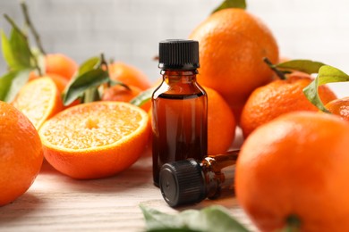 Photo of Bottles of tangerine essential oil and fresh fruits on wooden table, closeup
