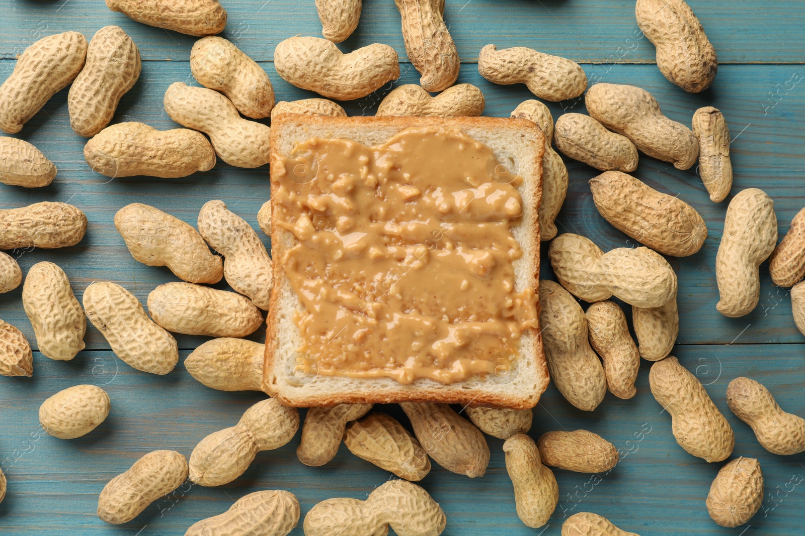 Photo of Delicious toast with peanut butter and nuts on light blue wooden table, flat lay