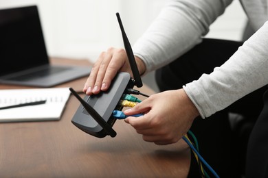 Photo of Man inserting cable into Wi-Fi router at wooden table indoors, closeup