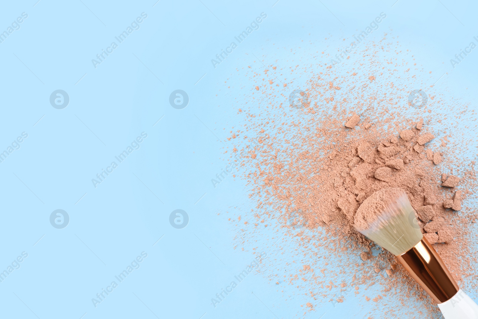 Photo of Makeup brush and scattered face powder on light blue background, top view. Space for text