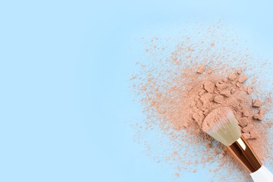 Makeup brush and scattered face powder on light blue background, top view. Space for text