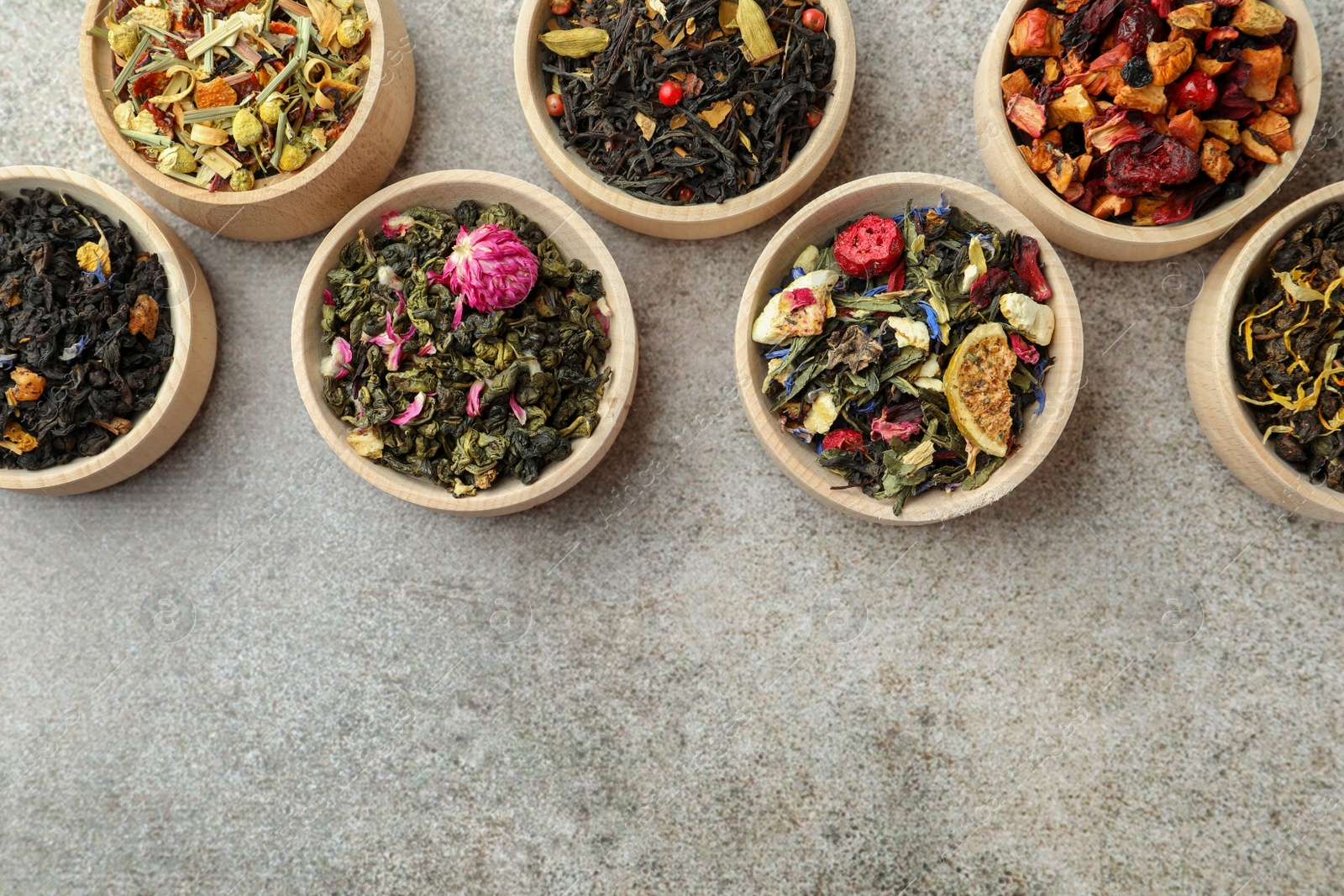 Photo of Different kinds of dry herbal tea in wooden bowls on light grey table, flat lay. Space for text