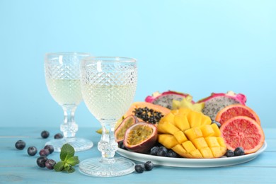 Delicious exotic fruits and wine on light blue wooden table