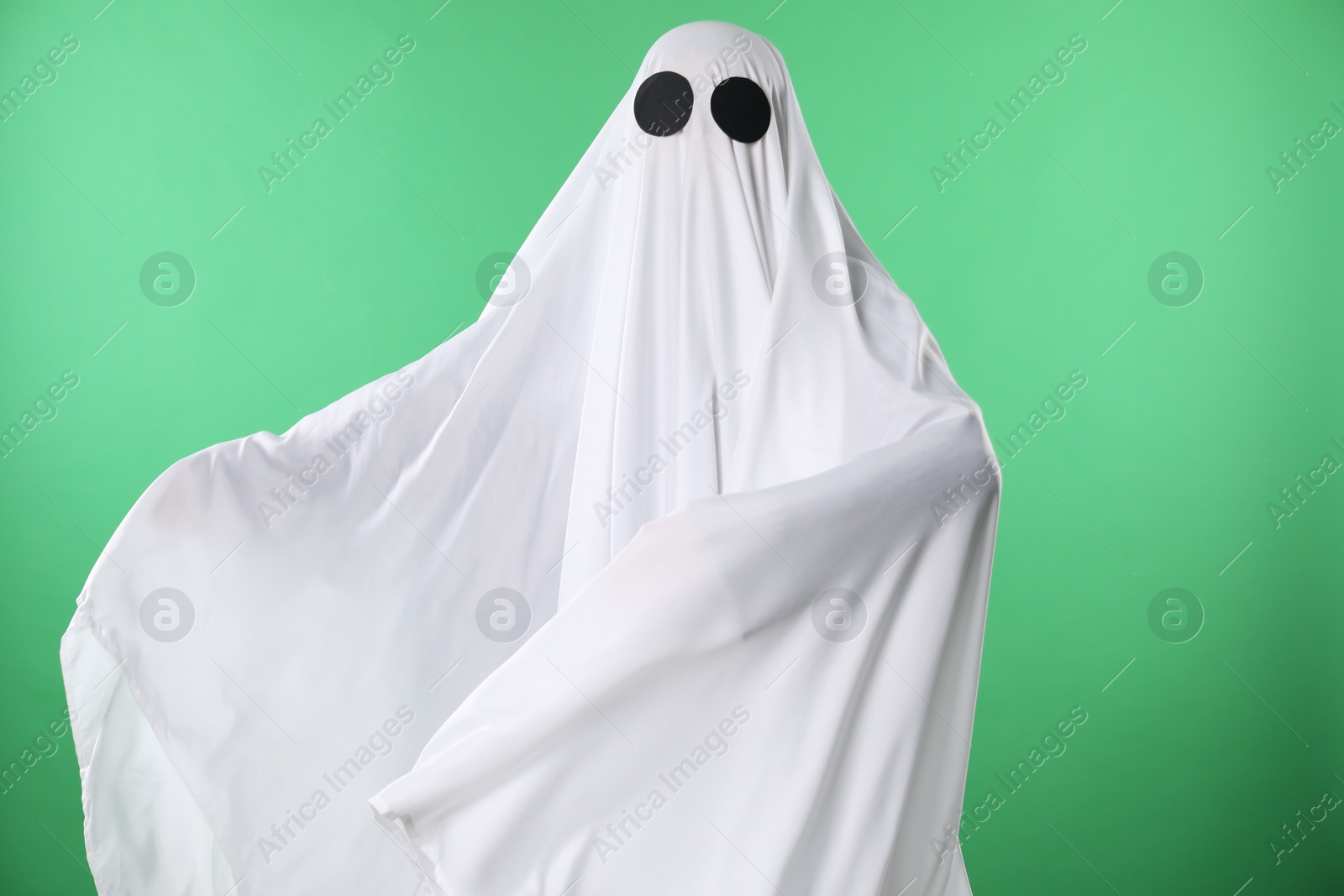 Photo of Creepy ghost. Person covered with white sheet on green background