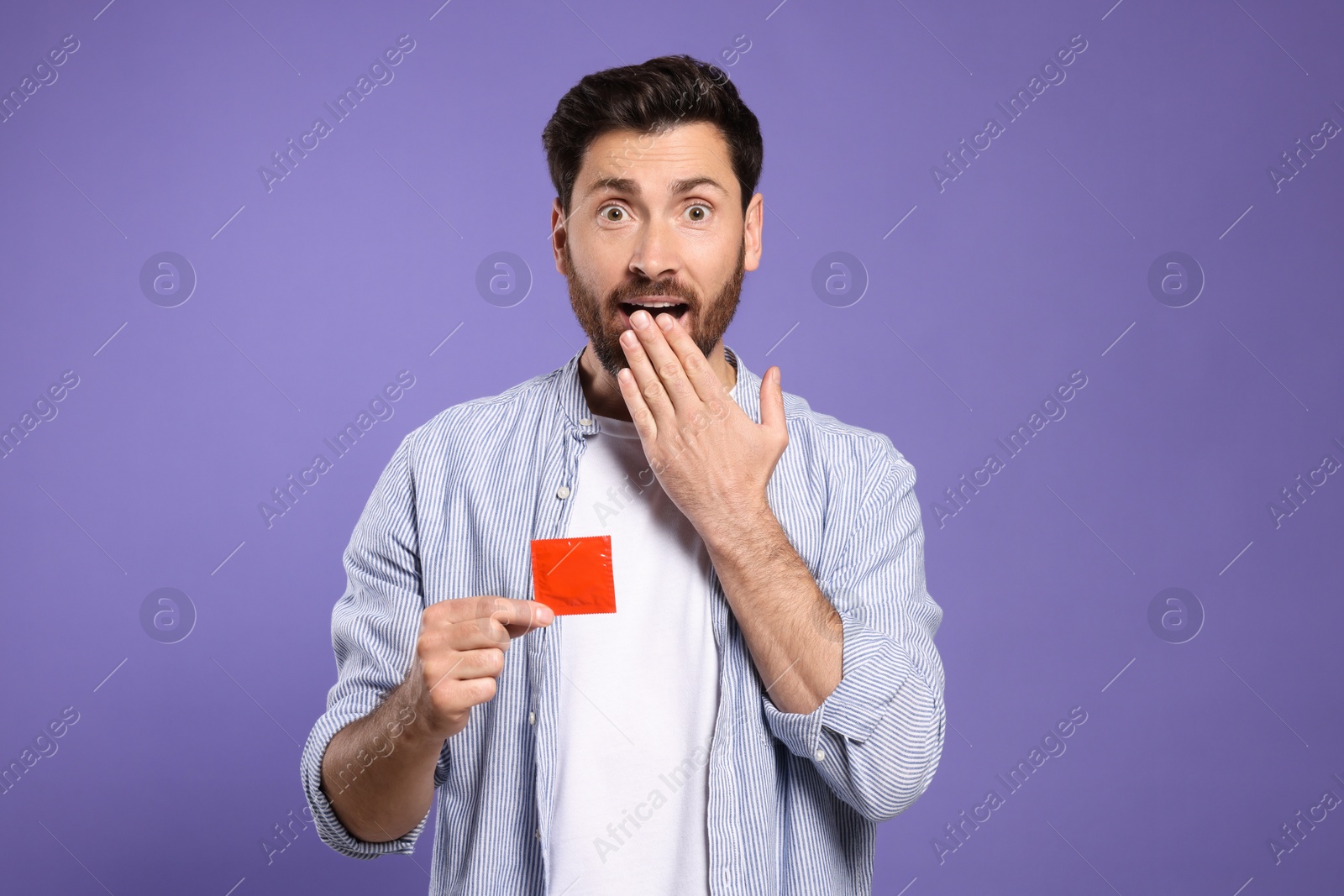 Photo of Emotional man holding condom on purple background. Safe sex