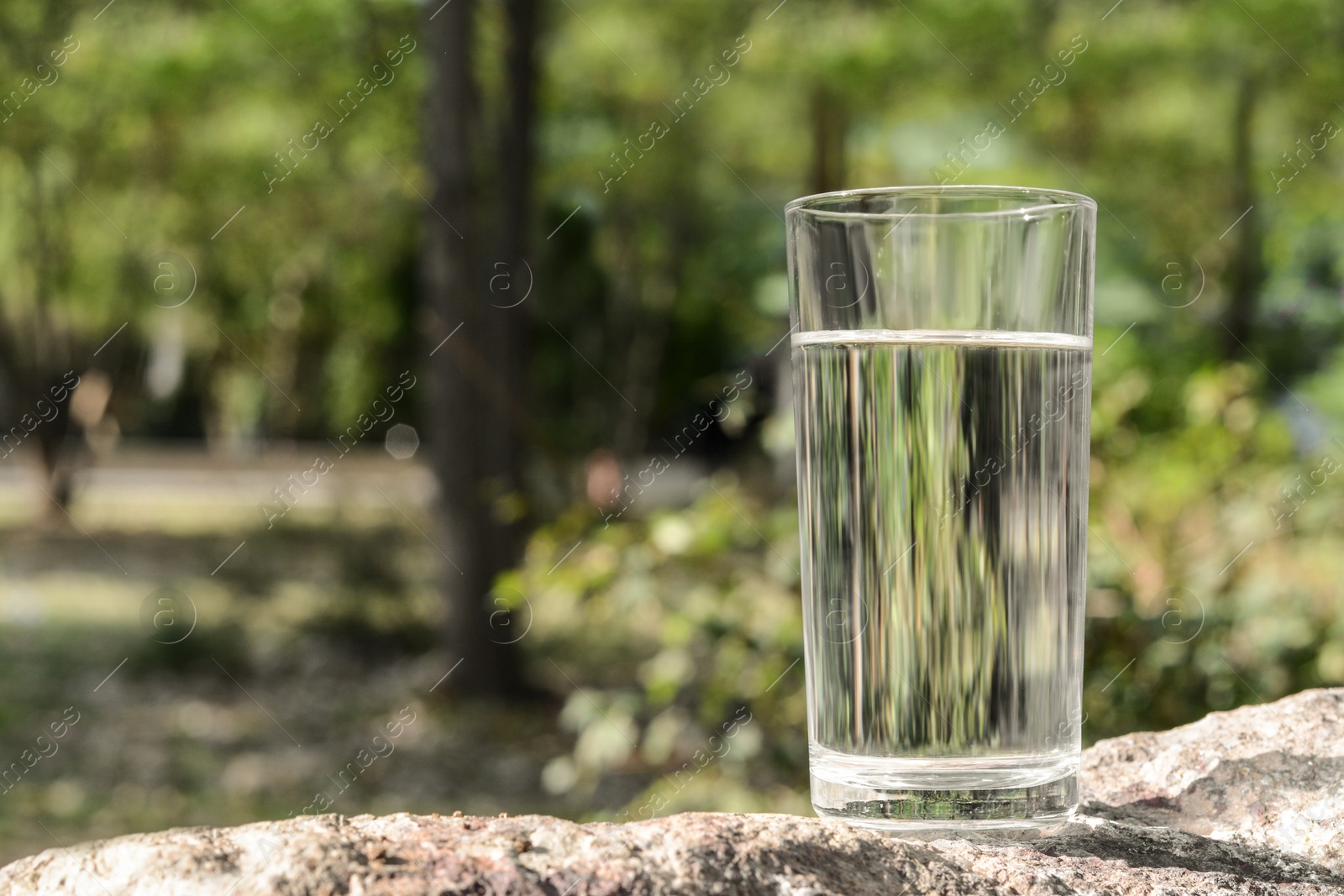 Photo of Glass of water on stone outdoors, space for text