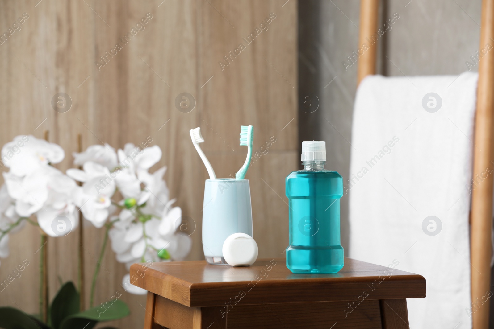 Photo of Bottle of mouthwash, toothbrushes and dental floss on wooden table in bathroom