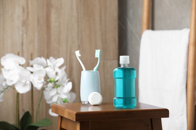 Bottle of mouthwash, toothbrushes and dental floss on wooden table in bathroom