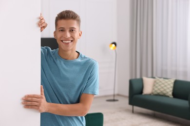 Photo of Happy man standing near white wall at home, space for text. Invitation to come in room