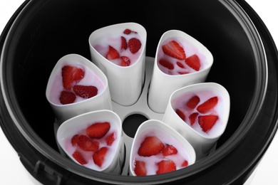 Photo of Cups of homemade strawberry yogurt in modern multi cooker on white background