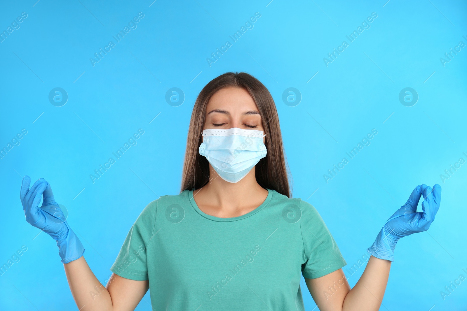 Photo of Woman in protective mask meditating on light blue background. Dealing with stress caused by COVID‑19 pandemic