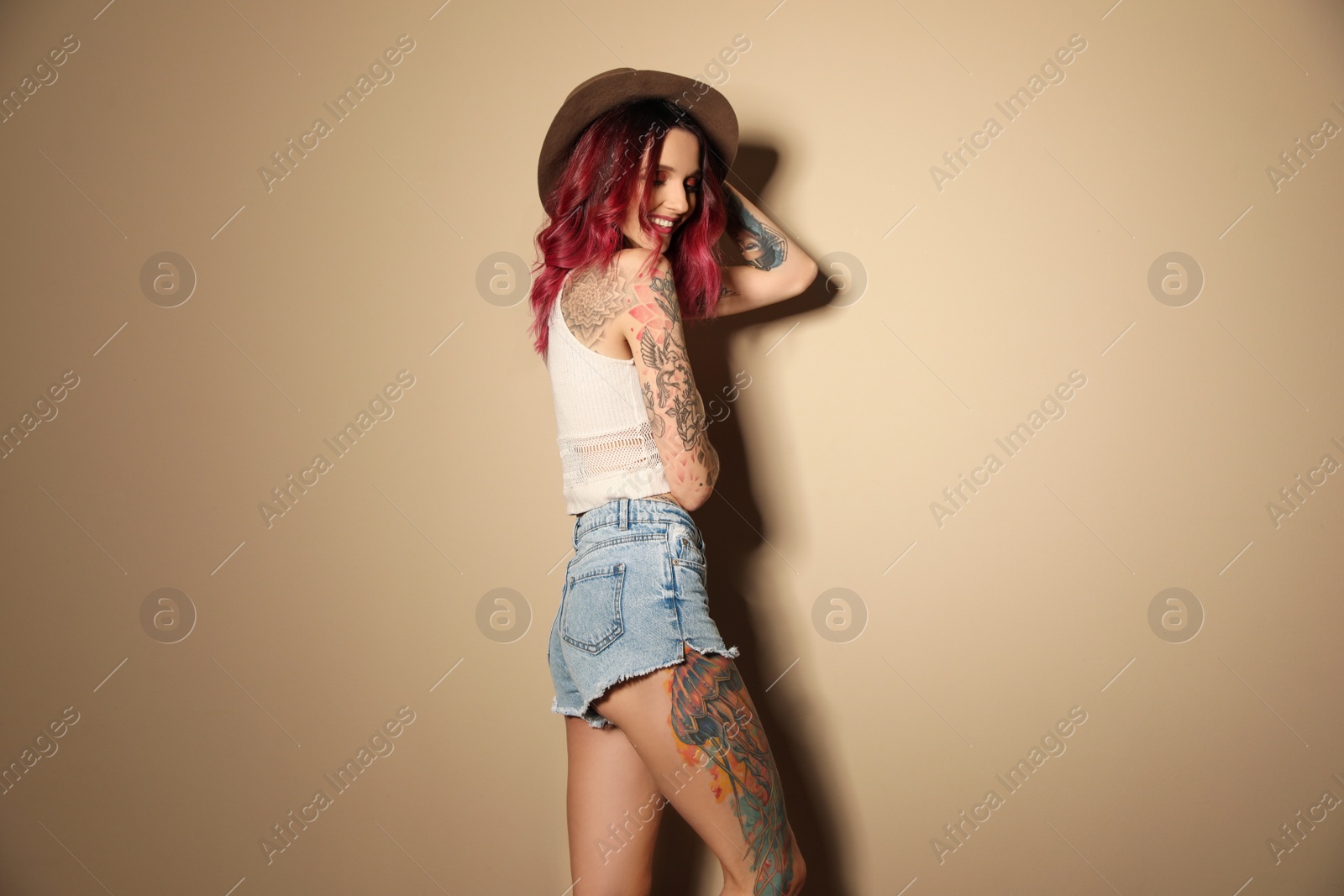 Photo of Beautiful woman with tattoos on body against beige background