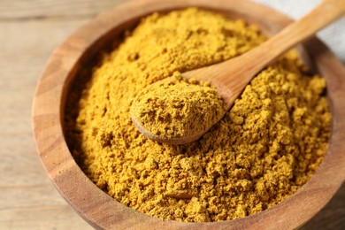 Photo of Dry curry powder in bowl and spoon on wooden table, closeup