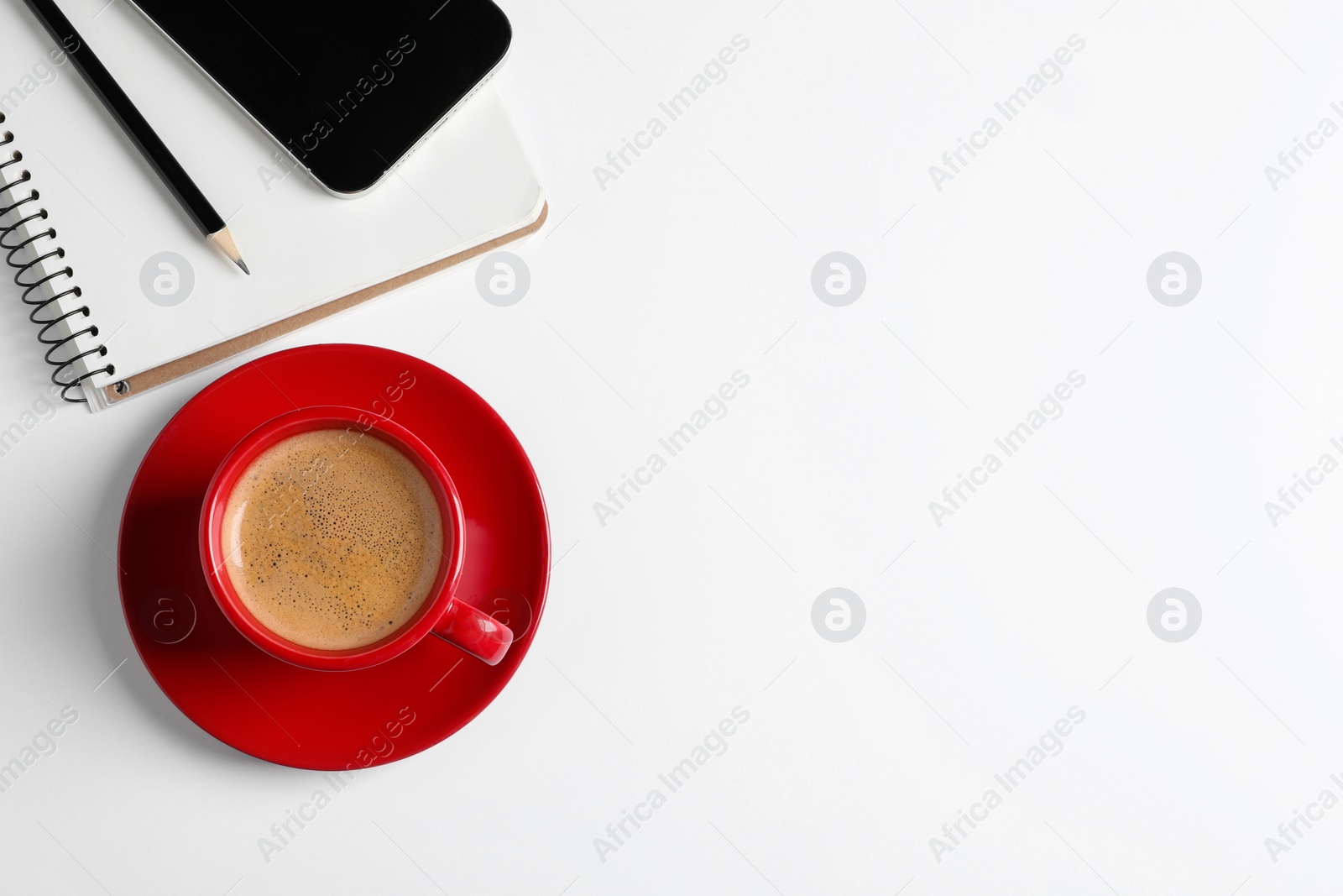 Photo of Red ceramic cup with hot aromatic coffee, notebook and smartphone on white background, flat lay. Space for text