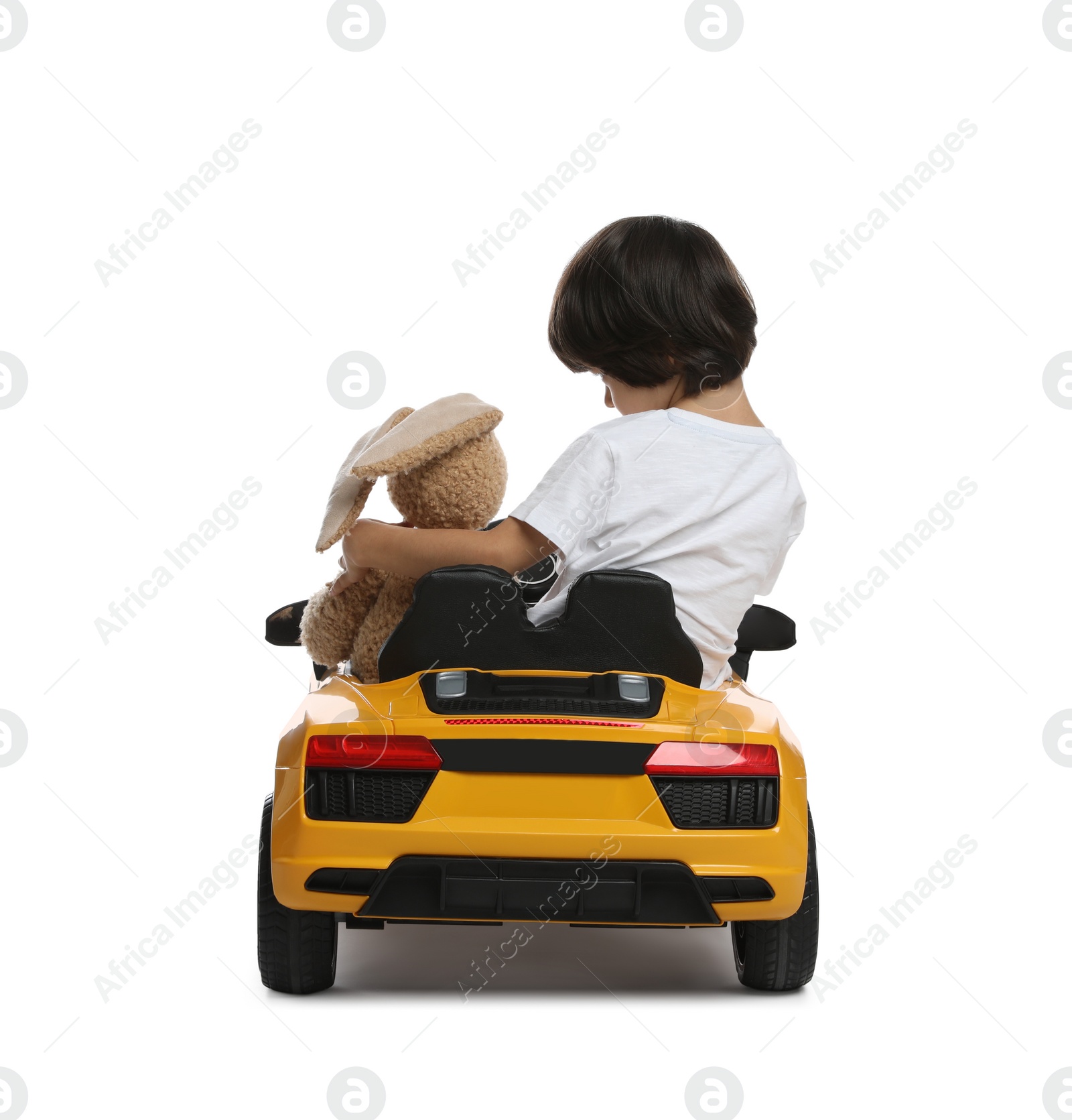 Photo of Cute little boy with toy bunny driving children's car on white background, back view