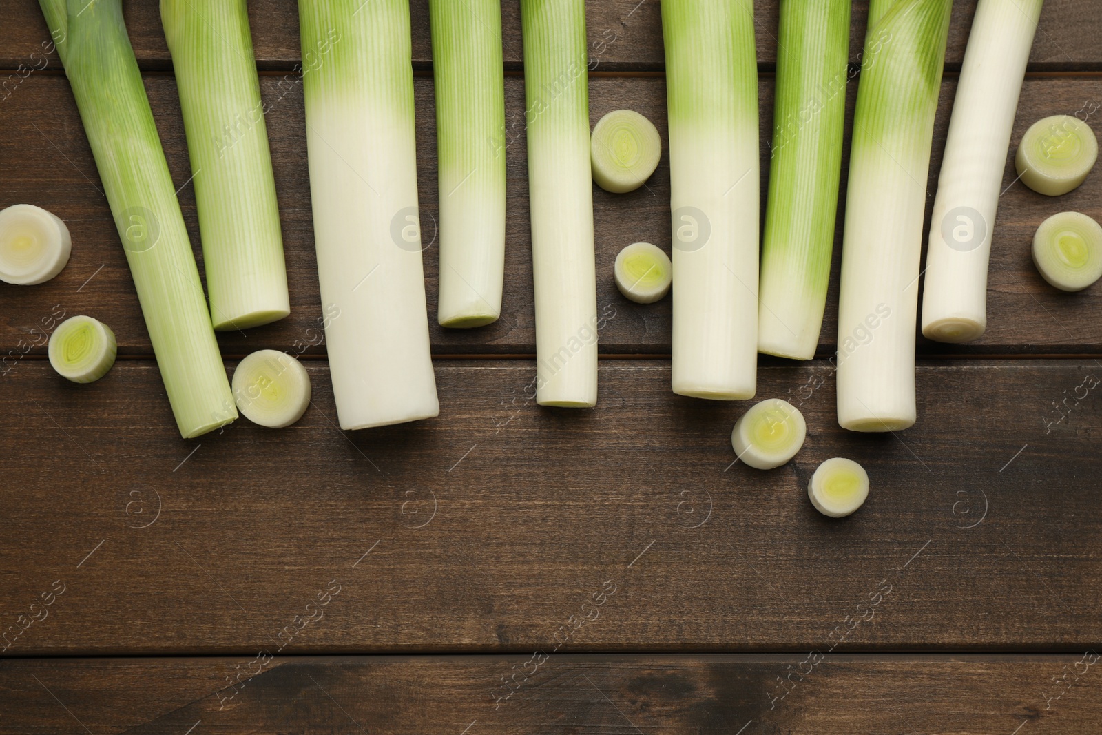 Photo of Whole and cut fresh leeks on wooden table, flat lay. Space for text