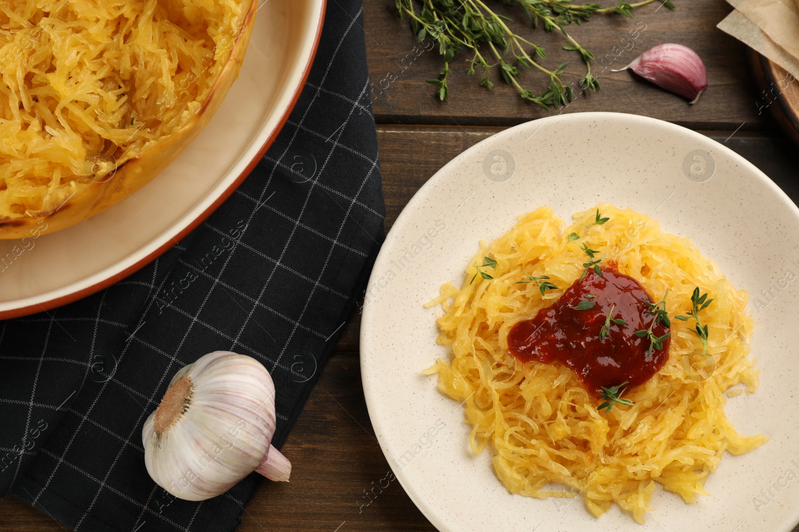 Photo of Tasty spaghetti squash with tomato sauce and thyme served on wooden table, flat lay