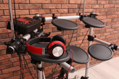 Photo of Modern electronic drum kit with headphones near red brick wall indoors. Musical instrument