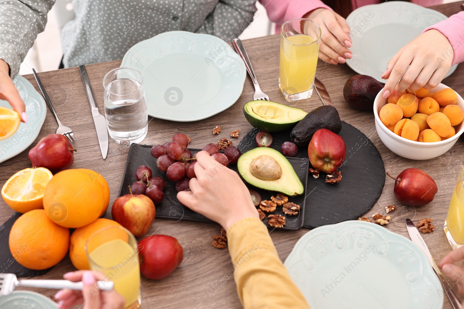 Photo of Friends eating vegetarian food at wooden table indoors, closeup