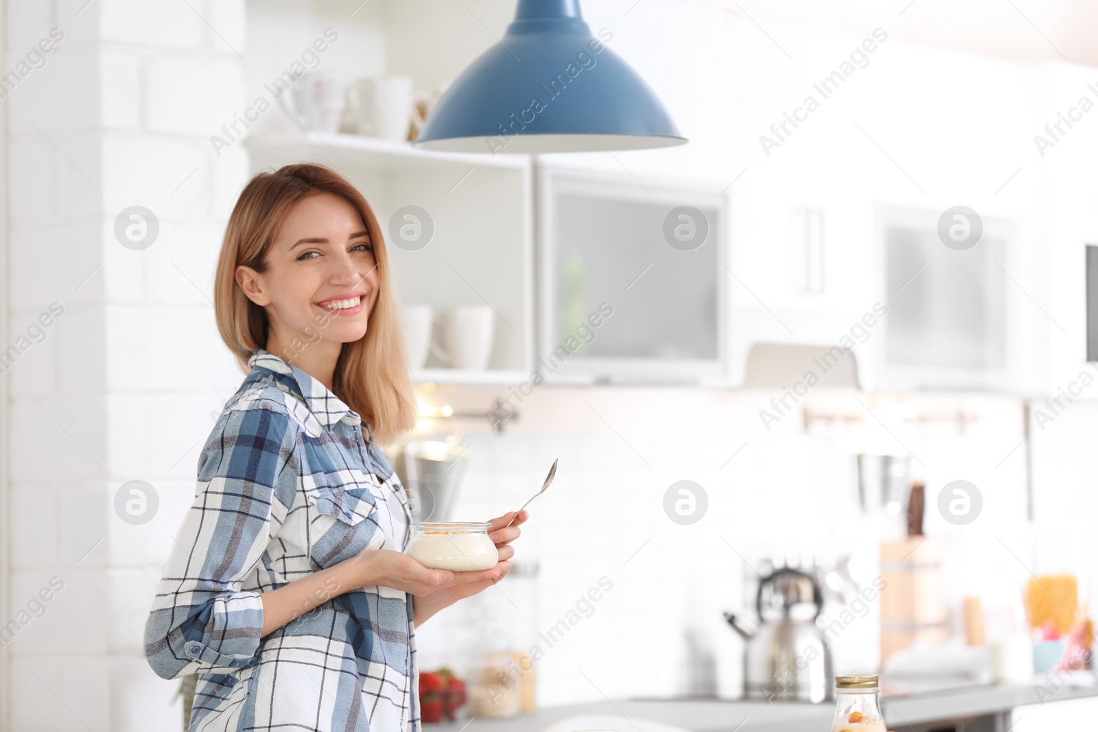 Photo of Young attractive woman eating tasty yogurt in kitchen