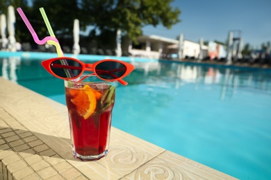 Photo of Tasty refreshing cocktail and sunglasses on edge of swimming pool. Party items