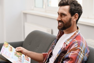 Photo of Smiling bearded man with magazine on sofa indoors