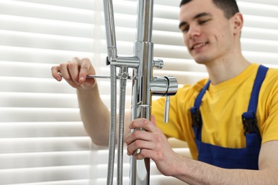 Photo of Smiling plumber repairing faucet with spanner in bathroom, selective focus