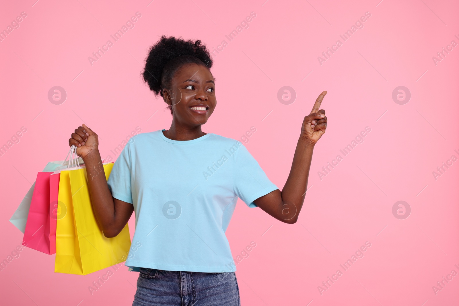 Photo of Happy young woman with shopping bags pointing at something on pink background. Space for text