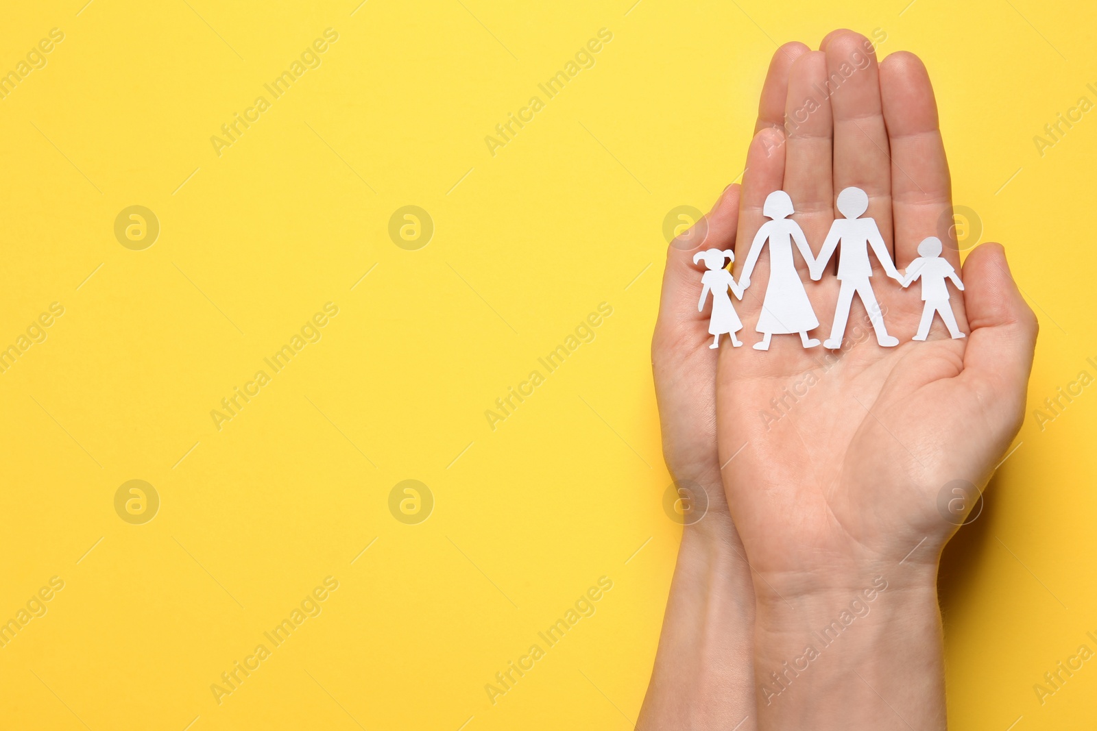 Photo of Woman holding paper cutout of family on yellow background, top view. Space for text