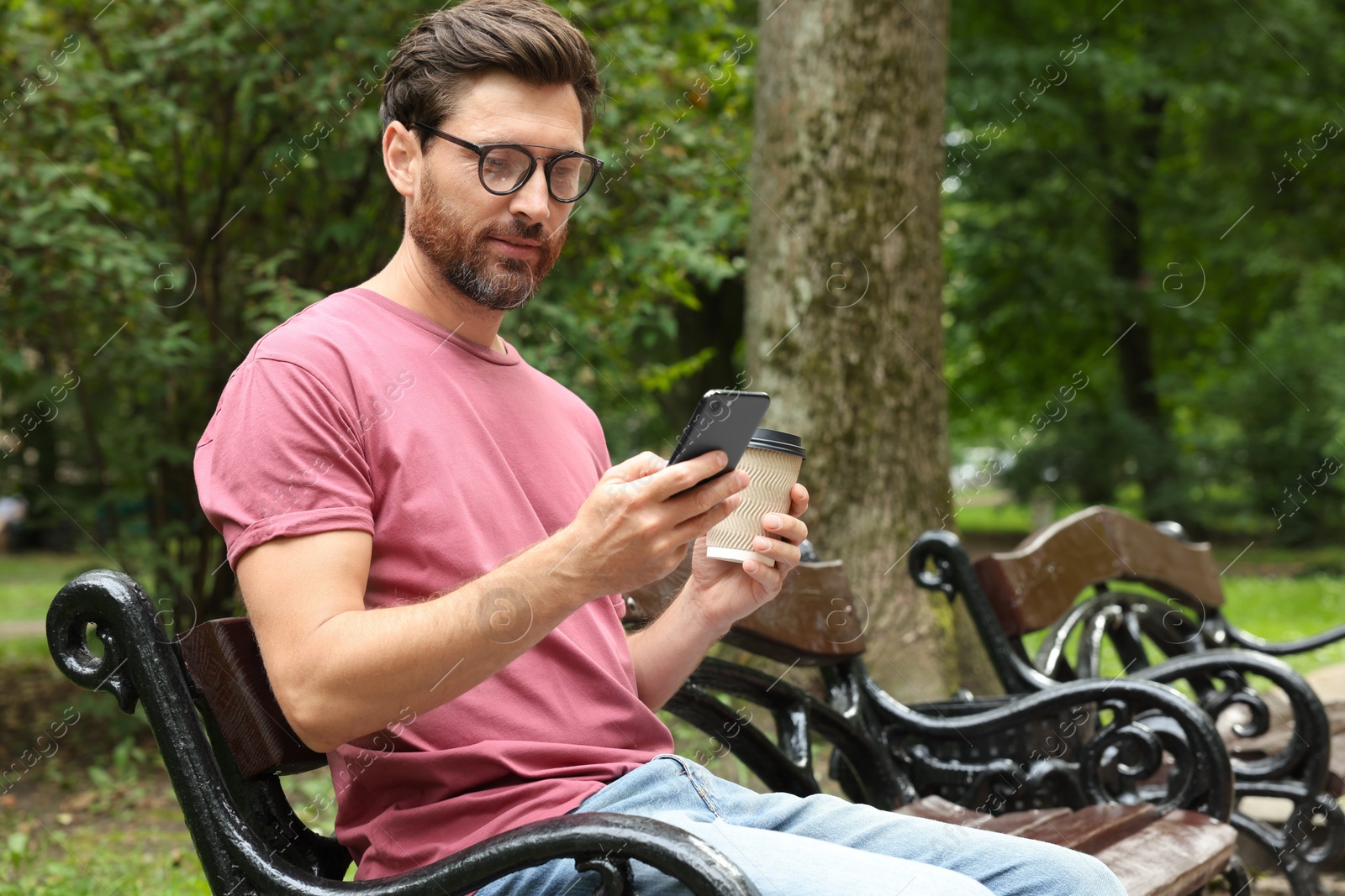 Photo of Handsome man with coffee using smartphone in park, space for text