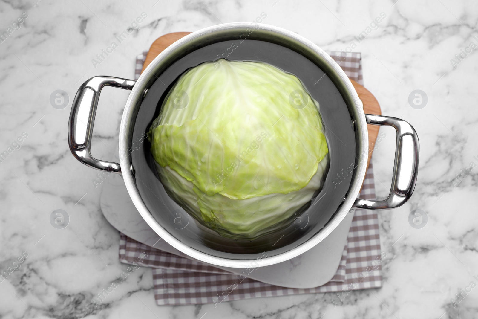 Photo of Sauce pan with hot water and cabbage for preparing stuffed rolls on white marble table, top view