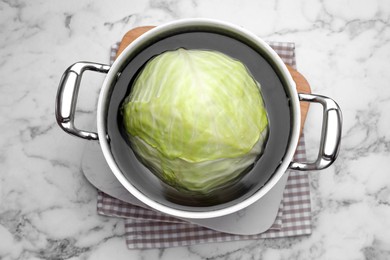 Sauce pan with hot water and cabbage for preparing stuffed rolls on white marble table, top view