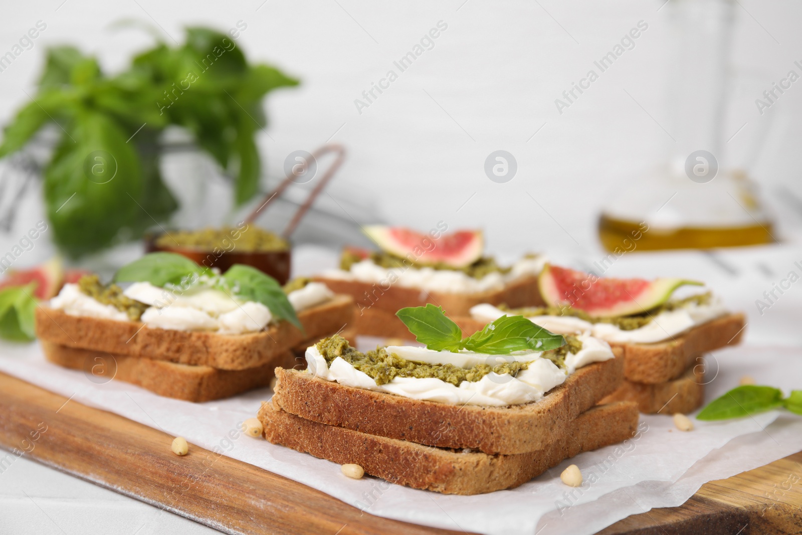 Photo of Tasty bruschetta with cream cheese, pesto sauce and fresh basil on parchment paper, closeup