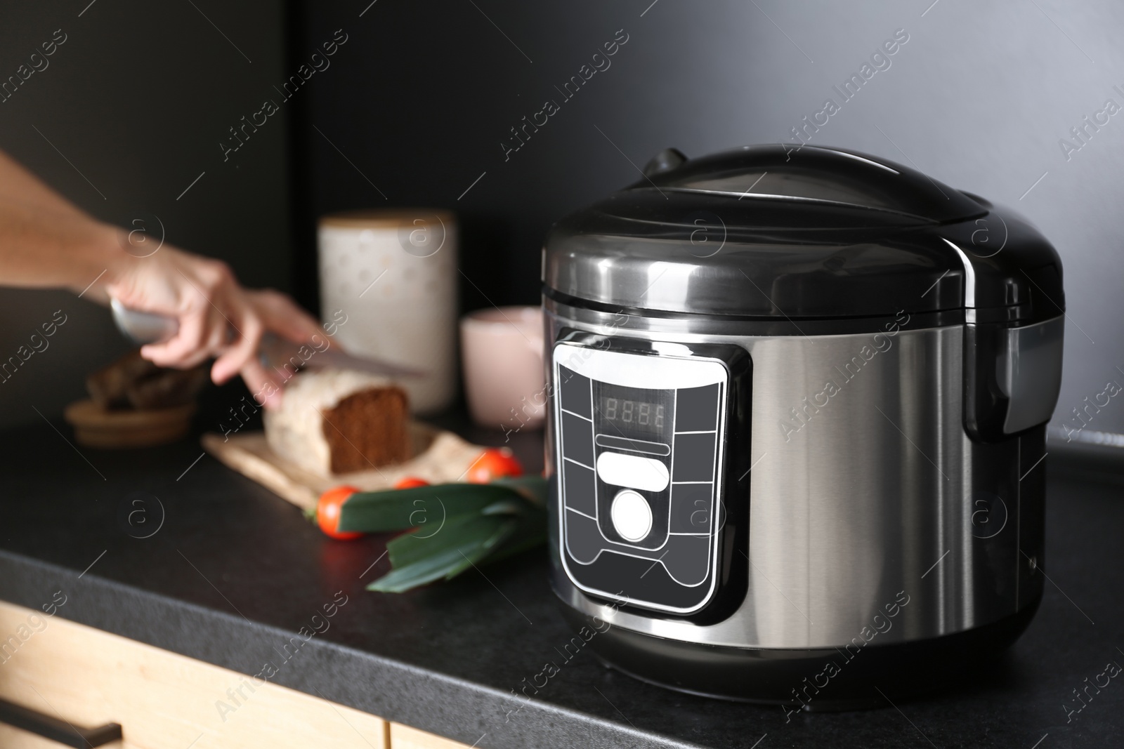 Photo of Modern multi cooker and woman slicing bread on table in kitchen, space for text
