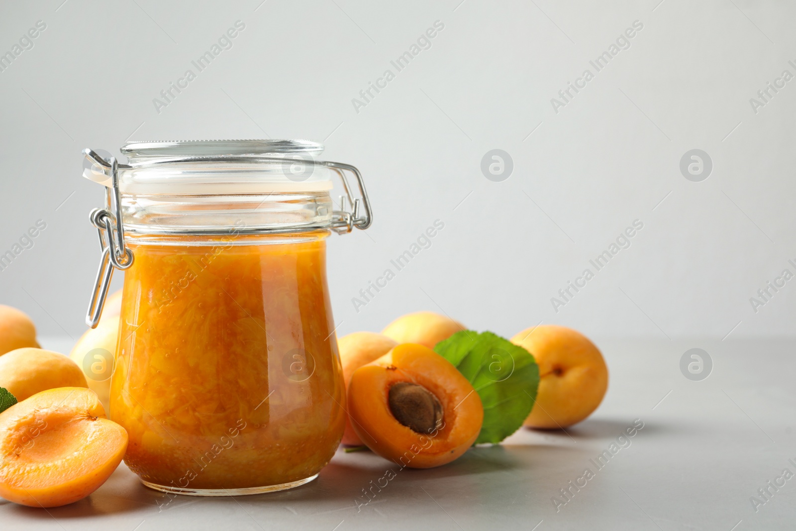 Photo of Jar of apricot jam and fresh fruits on light table. Space for text