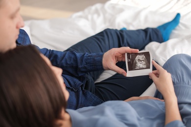 Photo of Young pregnant couple with ultrasound photo of their baby at home