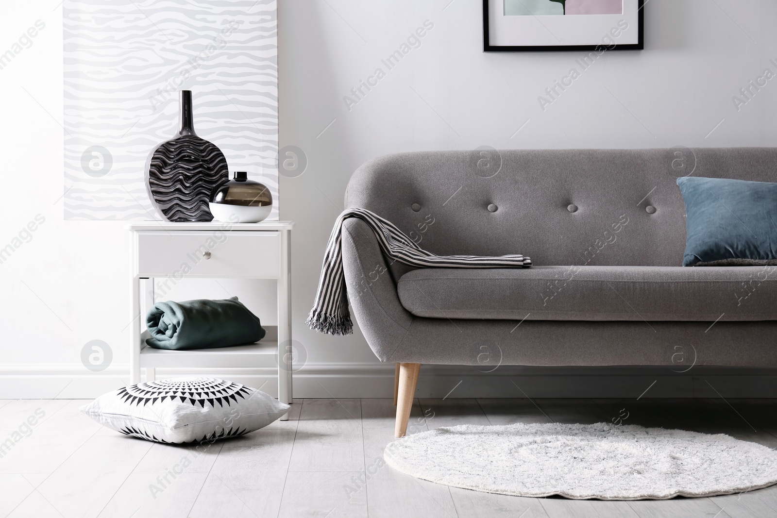 Photo of Living room interior with vases on side table and comfortable sofa near white wall